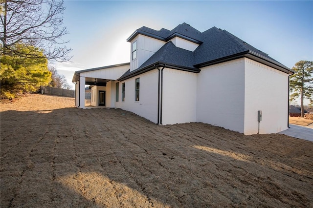 rear view of property featuring a shingled roof, brick siding, and fence