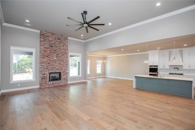 unfurnished living room featuring crown molding, light wood-style floors, a brick fireplace, baseboards, and ceiling fan with notable chandelier