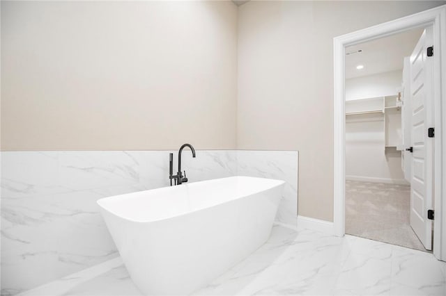 full bath with recessed lighting, marble finish floor, wainscoting, a soaking tub, and a walk in closet