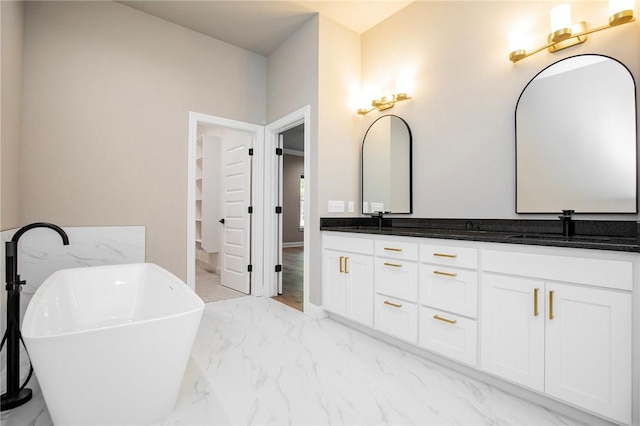 full bathroom with double vanity, marble finish floor, a freestanding bath, and a sink