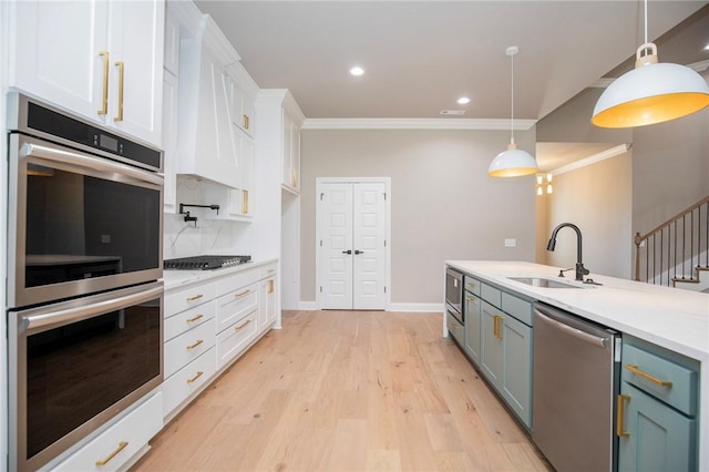 kitchen with light wood-style flooring, stainless steel appliances, a sink, white cabinets, and crown molding