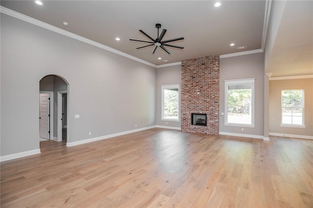 unfurnished living room featuring light wood finished floors, baseboards, arched walkways, crown molding, and a fireplace