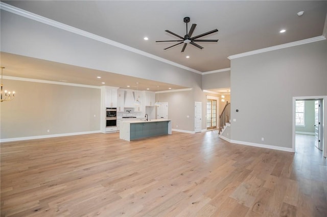 unfurnished living room featuring a wealth of natural light, light wood finished floors, baseboards, and ceiling fan with notable chandelier