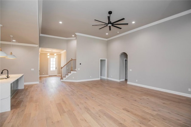 unfurnished living room featuring light wood-style flooring, arched walkways, baseboards, and ceiling fan with notable chandelier