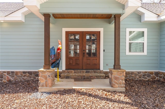 entrance to property featuring stone siding, french doors, and roof with shingles