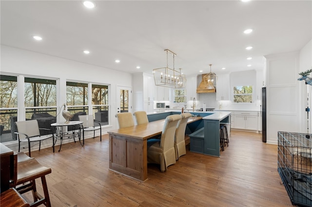 kitchen with a kitchen island with sink, premium range hood, wood finished floors, white cabinetry, and light countertops