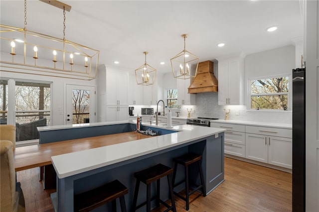 kitchen with stainless steel electric stove, light countertops, custom range hood, decorative backsplash, and a sink