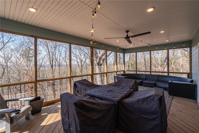 sunroom with a ceiling fan, a wooded view, and track lighting