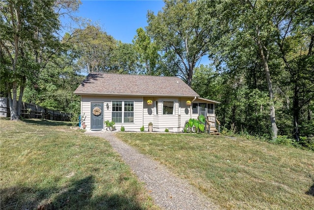 ranch-style house featuring a shingled roof, fence, and a front lawn