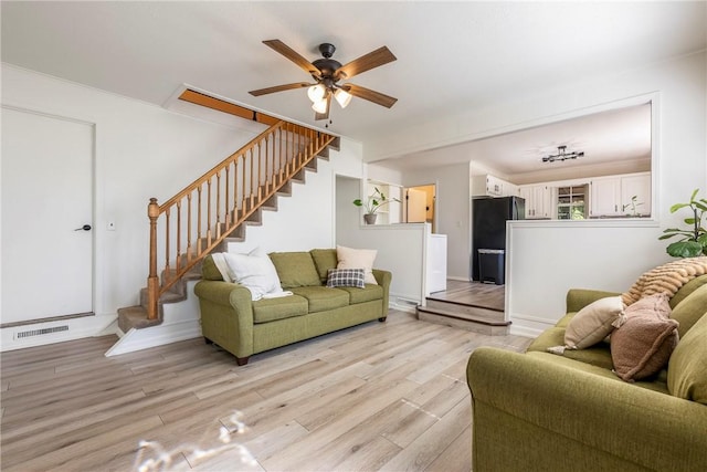 living area with light wood-style flooring, visible vents, baseboards, stairs, and a ceiling fan