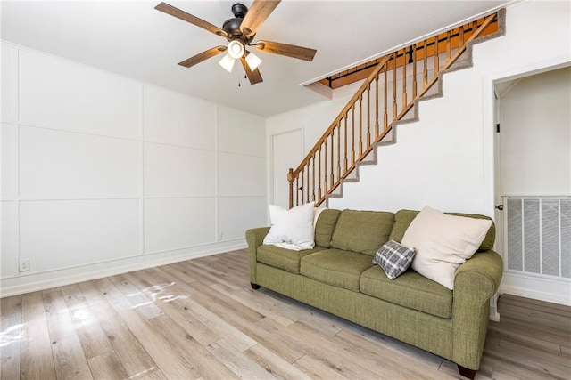 living area featuring a ceiling fan, visible vents, stairway, and wood finished floors