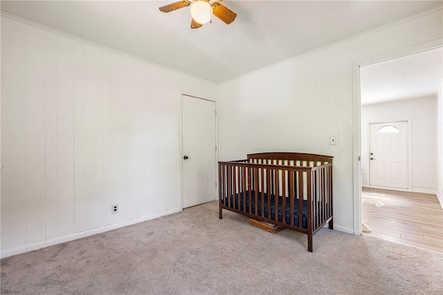 carpeted bedroom with a nursery area, ceiling fan, baseboards, and crown molding