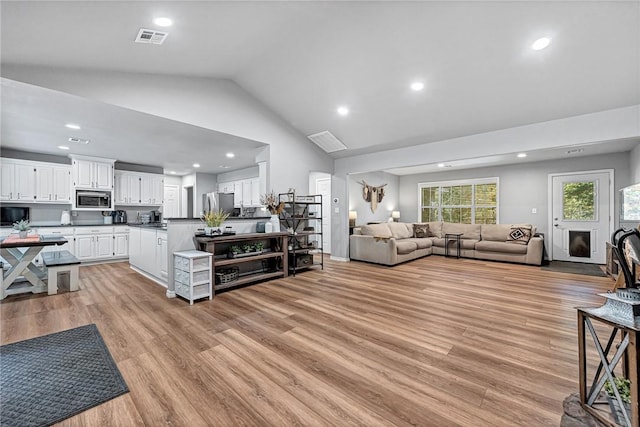 living room featuring high vaulted ceiling, light wood-type flooring, visible vents, and recessed lighting