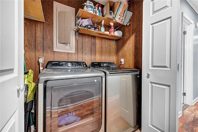 washroom with laundry area, electric panel, wooden walls, washer and clothes dryer, and light wood-style flooring