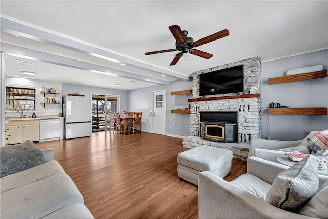 living area featuring a stone fireplace, wood finished floors, visible vents, a ceiling fan, and beamed ceiling