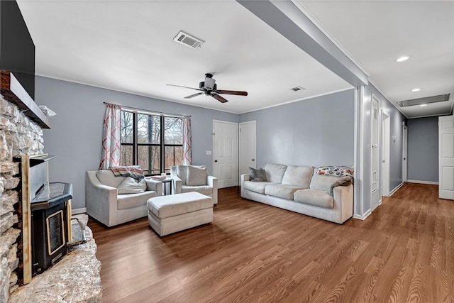 living area with visible vents, ceiling fan, ornamental molding, wood finished floors, and a wood stove