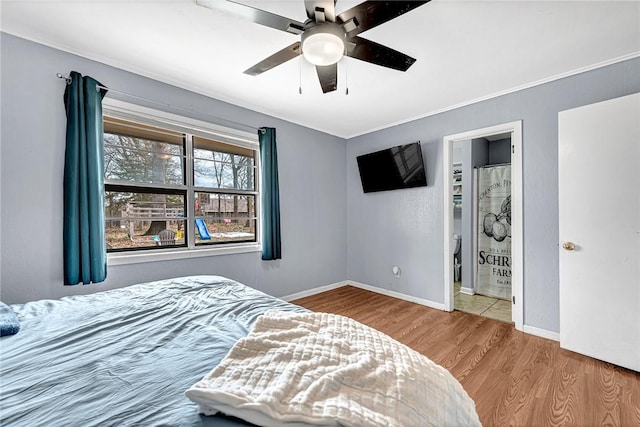 bedroom featuring ceiling fan, wood finished floors, baseboards, ensuite bath, and crown molding