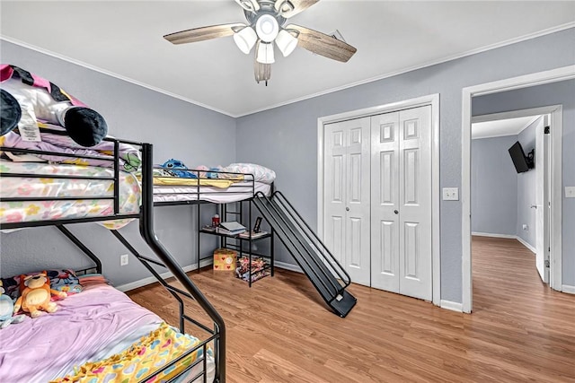 bedroom with baseboards, a closet, wood finished floors, and crown molding