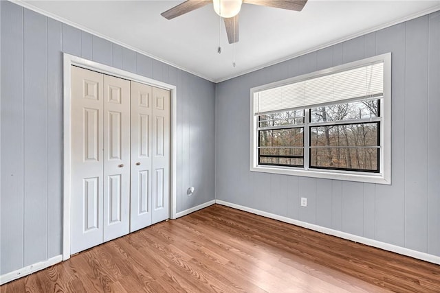 unfurnished bedroom featuring ceiling fan, wood finished floors, baseboards, ornamental molding, and a closet