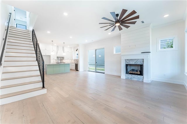 unfurnished living room with light wood-style flooring, recessed lighting, a premium fireplace, baseboards, and stairs