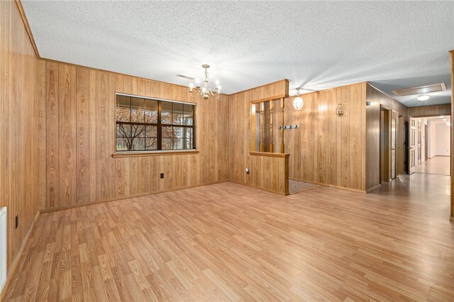 spare room featuring a notable chandelier, visible vents, a textured ceiling, wood finished floors, and baseboards