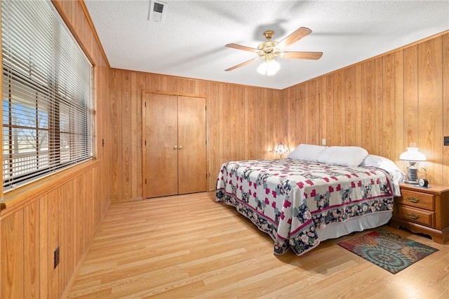 bedroom with light wood-type flooring, visible vents, wooden walls, and a textured ceiling