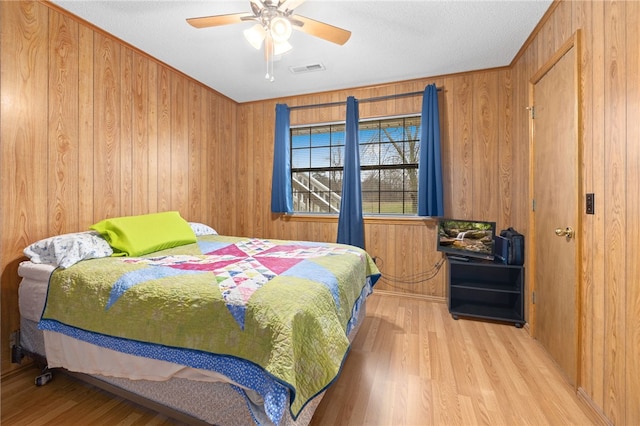 bedroom featuring visible vents, ceiling fan, wooden walls, and wood finished floors