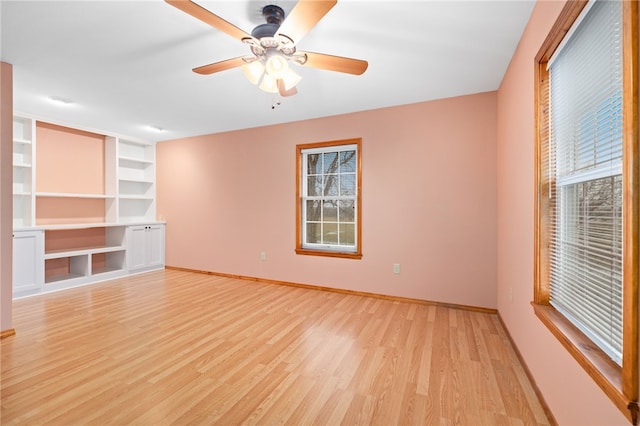 spare room featuring a ceiling fan, light wood-type flooring, built in shelves, and baseboards