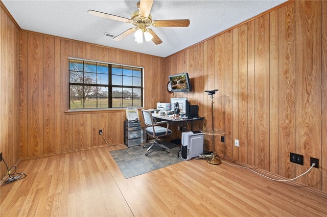 office with a textured ceiling, wooden walls, wood finished floors, visible vents, and a ceiling fan