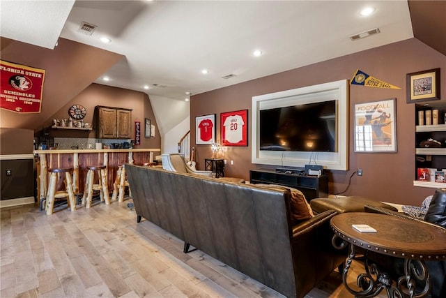 living room with visible vents, vaulted ceiling, light wood-style flooring, and a bar