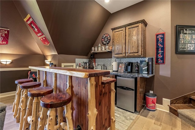 bar featuring refrigerator, indoor wet bar, lofted ceiling, decorative backsplash, and light wood-type flooring