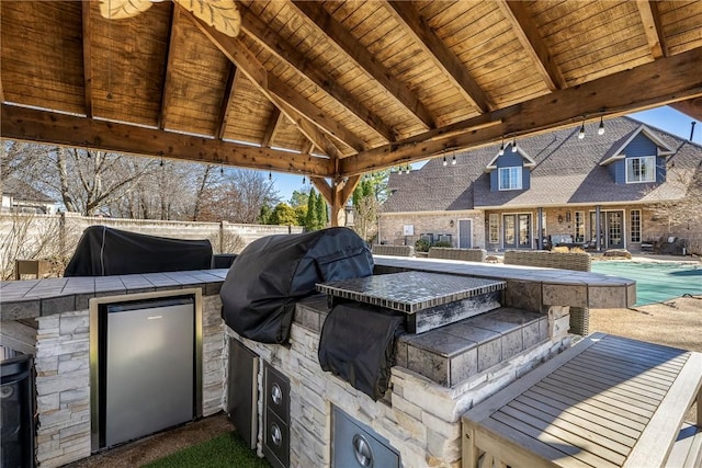 view of patio with area for grilling, an outdoor kitchen, fence, and a fenced in pool