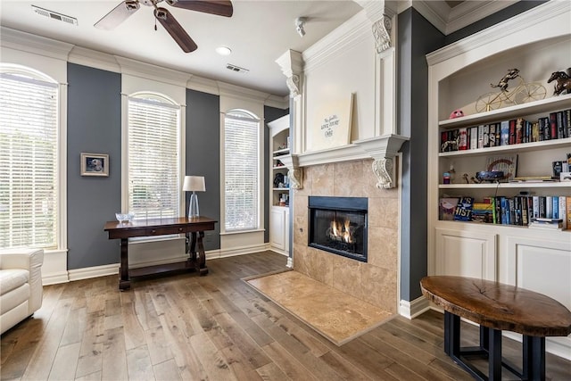 sitting room featuring crown molding, a tiled fireplace, visible vents, and wood finished floors