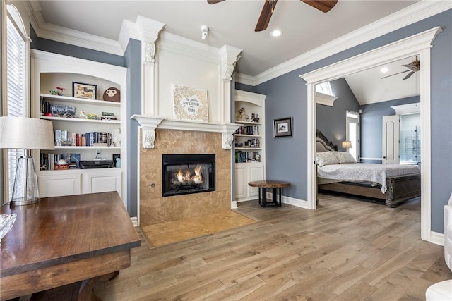 bedroom featuring light wood finished floors, multiple windows, a tile fireplace, and crown molding