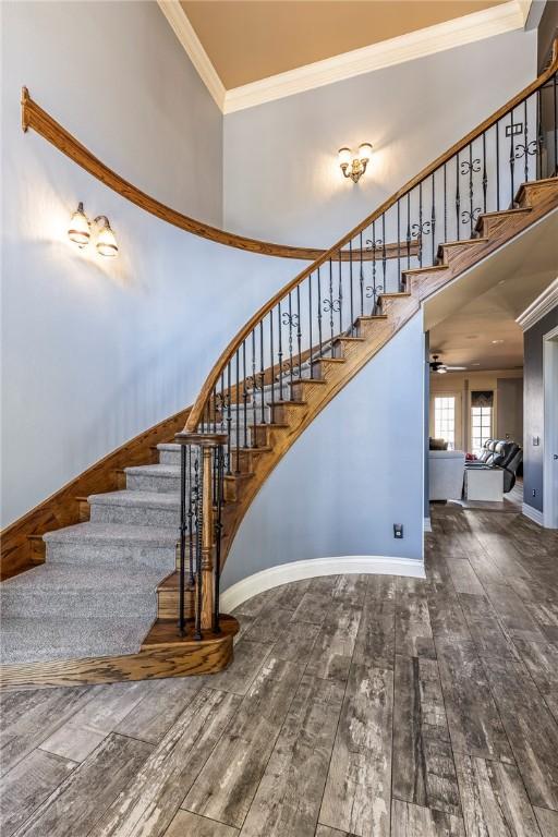 stairs featuring baseboards, hardwood / wood-style floors, a high ceiling, and crown molding