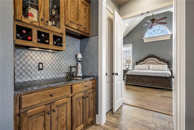 interior space with light wood-style flooring, decorative backsplash, a sink, vaulted ceiling, and ceiling fan