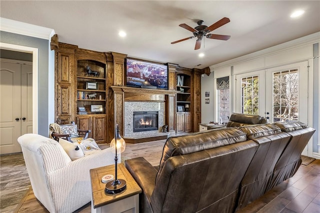 living area featuring ceiling fan, wood finished floors, french doors, a glass covered fireplace, and crown molding