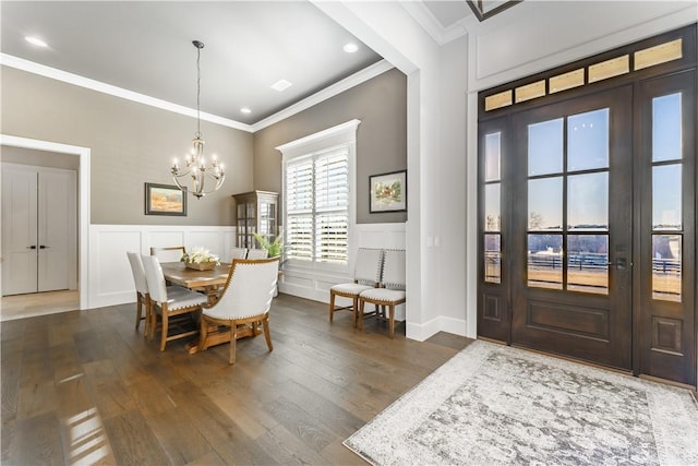 dining area featuring ornamental molding, a chandelier, dark wood finished floors, wainscoting, and a decorative wall