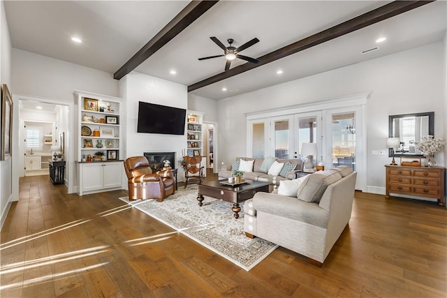 living area with dark wood-style floors, french doors, visible vents, a glass covered fireplace, and beamed ceiling