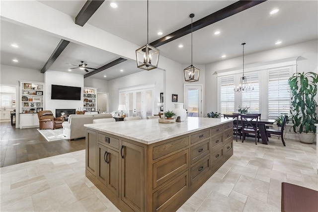 kitchen featuring light stone counters, beamed ceiling, a glass covered fireplace, and decorative light fixtures