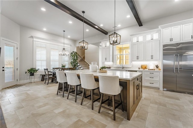 kitchen featuring stainless steel built in fridge, a chandelier, beamed ceiling, a large island, and stone tile flooring