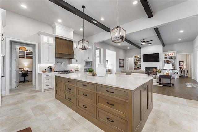 kitchen with white cabinets, beamed ceiling, stainless steel appliances, premium range hood, and a fireplace