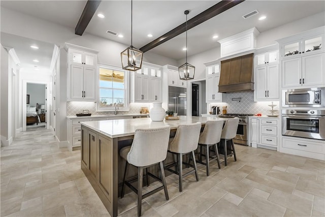 kitchen featuring stainless steel appliances, custom range hood, beamed ceiling, a spacious island, and backsplash