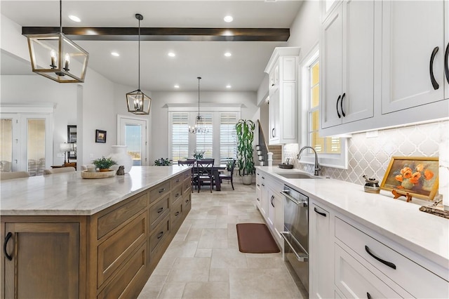 kitchen with an inviting chandelier, white cabinetry, backsplash, and a sink