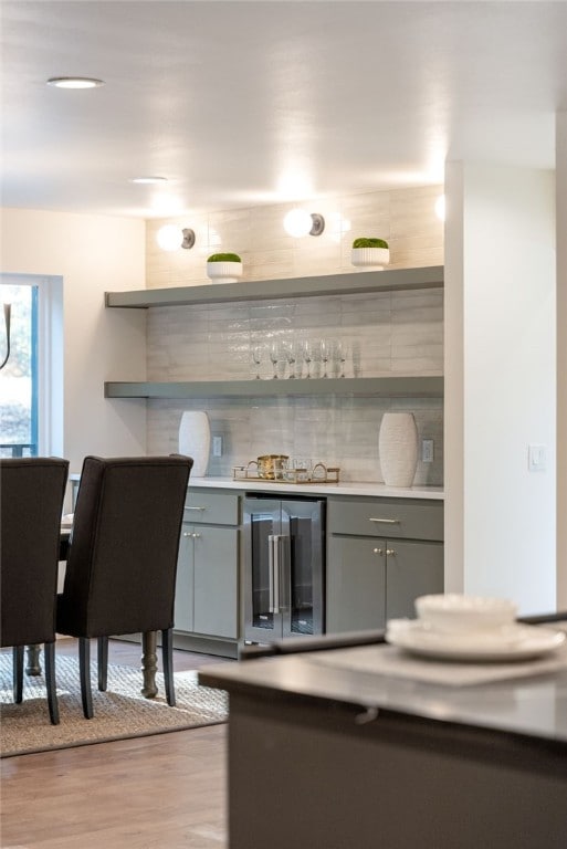 bar with beverage cooler, a dry bar, wood finished floors, and decorative backsplash