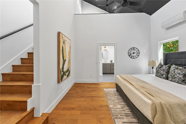 bedroom featuring a towering ceiling, light wood finished floors, baseboards, and an AC wall unit