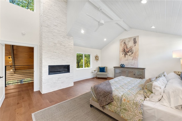 bedroom featuring baseboards, wood finished floors, a fireplace, high vaulted ceiling, and beam ceiling