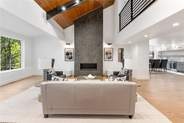 living area featuring wooden ceiling, light wood-style flooring, beverage cooler, a high end fireplace, and baseboards