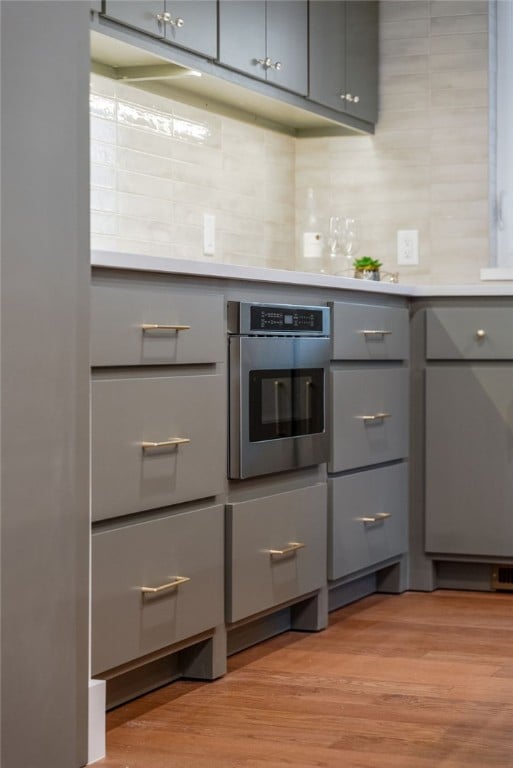 kitchen with light wood-style flooring, stainless steel oven, gray cabinets, and light countertops