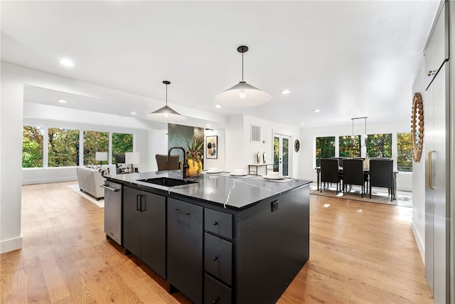 kitchen with dark countertops, light wood-style floors, open floor plan, a sink, and dark cabinetry